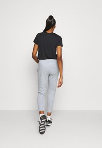 Schwarzes T-Shirt mit kurzen Ärmeln, graue Jogginghosen mit elastischem Bund, schmaler Schnitt, mit Seitentaschen, kombiniert mit schwarzen Turnschuhen und weißen Knöchelsocken.