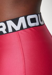 Rosa sportliche Shorts verfügen über einen schwarzen elastischen Bund mit weißem Text. Der Stoff hat eine glatte Textur und sichtbare Nahtdetails.
