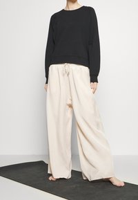 Felpa nera con design cropped e maniche lunghe, abbinata a pantaloni ampi di un beige chiaro con vita elasticizzata e coulisse.