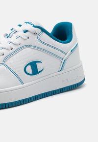 Vita sneakers med turkosa accenter, med en slät läderöverdel, robust sula, texturerad logotyp och kontrasterande sömmar.