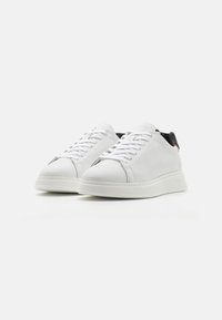 Ein Paar weiße Leder-Sneaker mit niedriger Spitze, weißen Schnürsenkeln und schwarzem Innenfutter auf einem weißen Hintergrund, schräg dargestellt, um die Vorder- und Seite zu zeigen.