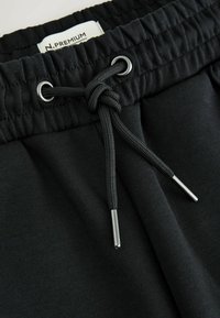 Black stretch fabric shorts with an elastic waistband, featuring a drawstring with silver metal tips and a tag labeled "N.PREMIUM."