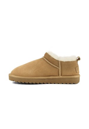 Chausson en daim beige à coupe basse avec semelle épaisse et doublure en polaire blanche, équipé d'une languette cousue au talon et d'une semelle extérieure en caoutchouc texturée.