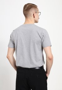 Grijs T-shirt met korte mouwen en een ronde hals, met een zachte textuur. Gecombineerd met zwarte broeken en een zwarte riem, gezien vanuit de achterkant.