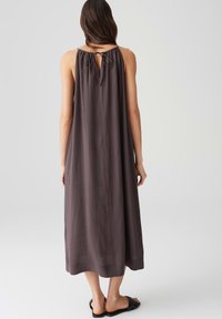 Ärmelloses, langes graues Kleid mit lockerer Passform, Schlüsselrücken-Detail und glatter Textur. Getragen mit einfachen schwarzen Sandalen.