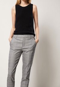 Zwart gebreid mouwloos topje gecombineerd met lichtgrijze geruite tailleropbroek. De broek heeft zijzakken en een gladde afwerking.