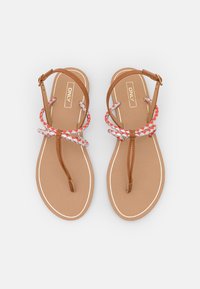 Brown flat sandals with braided red and white straps, a toe post design, and a light brown footbed featuring white trim along the sole.
