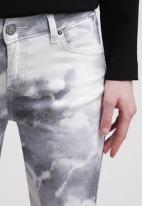 Bílé džíny s vysokým pasem a šedými vzory mraků. Mají zapínání na knoflík a přední kapsy. Jsou vyrobeny z denimu s hladkým povrchem.