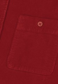 Primo piano di un tessuto in corduroy rosso che mostra una tasca quadrata con un bottone rosso abbinato cucito vicino al centro superiore.