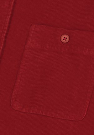 Nahaufnahme von rotem Cordstoff, der eine quadratische Tasche mit einem passenden roten Knopf zeigt, der nahe der oberen Mitte angenäht ist.