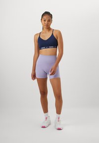 Marine sports-bh med hvit logo-bånd, kombinert med lavendel høytlivshorts. Modell iført hvite sko med rosa detaljer.