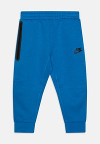 Sininen puuvillasekoitehousu, jossa on joustava vyötärö, sivuvetoketjullinen tasku ja musta Nike-logo oikeassa lahkeessa.