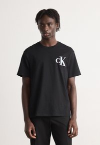 Svart bomull t-skjorte med korte ermer som har en hvit "ck" logo på venstre bryst. Enkelt design, avslappet passform, myk tekstur.
