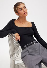 Maglietta nera a maniche lunghe con scollatura quadrata, abbinata a pantaloni grigi a vita alta. L'outfit presenta una cintura nera e un tessuto testurizzato.