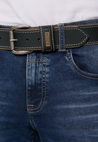 Dunkle Denim-Jeans verfügen über eine sichtbare Taschennäht und Kontrastnähte. Ein schwarzer Ledergürtel mit einer silbernen Schnalle fixiert den Bund.
