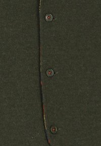 Maglione verde scuro con un'armatura a maglia testurizzata, caratterizzato da cinque bottoni grigi e cuciture multicolori lungo la patta dei bottoni.