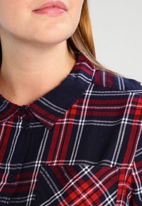 Marineblauw en rood geruit overhemd met witte strepen en knopen. Voorzien van een kraag en knopen aan de voorkant, gemaakt van geweven stof met een gestructureerde afwerking.