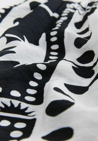 Svart och vitt tyg med abstrakta mönster som inkluderar cirklar och former. Materialet verkar lätt och texturerat, med en flödande drapering.