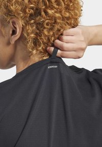 Juoda sportinė marškinė su tekstūruota medžiaga. Etiketėje užrašas "AEROREADY" ir kilpelė kabinimui, matoma nugaros kaklo dalyje.
