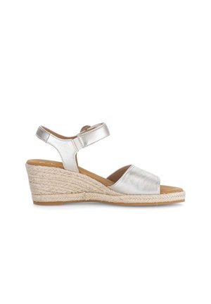 Zilveren sleehak sandaal met open teen, enkelriem en gevlochten jute plateauzool tegen een witte achtergrond.