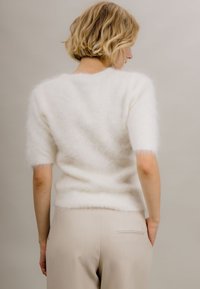 Myk hvit kortermet genser med myk tekstur, tettsittende silhuett og rund hals. Kombinert med lysebeige høytlivsbukser.