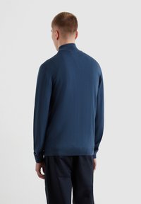 Pull noir à manches longues avec un col montant, fabriqué en tissu tricoté texturé. Comprend un ourlet droit et des poignets ajustés.
