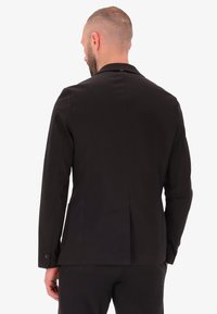 Giacca nera su misura con un'unica fessura sul retro e dettagli a bottone sulle maniche. Tessuto liscio con una vestibilità strutturata.