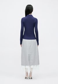 Bluză albastru închis cambrată cu mâneci lungi și guler, asortată cu o fustă gri, de lungime medie, având o deschizătură la spate și bordură din dantelă la tiv.