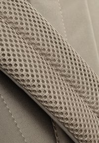 Tessuto beige texturizzato caratterizzato da una superficie tessuta liscia e una rete con ritagli circolari, che mette in mostra materiali a contrasto e cuciture sottili.