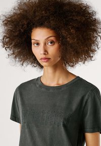 Tumehallist puuvillast T-särk, millel on lühikesed varrukad, ümmargune kaelus ning tekstuuriga graafiline disain kontrastse tooni jaoks.