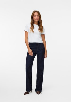 Vit kortärmad t-shirt matchad med mörkblå, raka jeans. Skorna är bruna med spetsiga tår och små detaljer. Släta tyger.