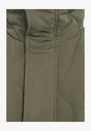 Dichtbijzicht van een olijfgroene gewatteerde jas, met zachte stof, afgeronde stikpatronen en een opvallende hoge kraag.