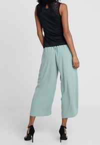 Haut noir sans manches avec des accents en dentelle sur les épaules, associé à un pantalon large couleur menthe claire. Des talons noirs complètent la tenue.