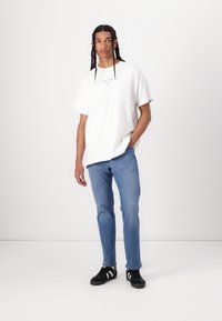 Hvid bomulds t-shirt med blå grafisk tekst, parret med lyseblå jeans og sorte sneakers med hvide striber.