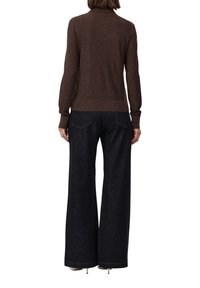 Maglione lavorato a maglia marrone con sottili spruzzi metallici, abbinato a pantaloni in denim neri a gamba larga con tasche posteriori e orlo grezzo.