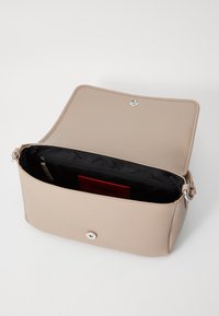 Bolso de mano de piel beige con una textura suave, herrajes plateados y un cierre magnético. El interior presenta un forro negro y un bolsillo con cremallera.