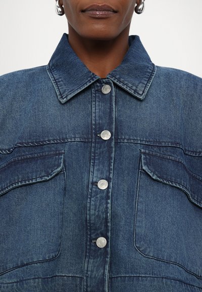 Jeans jakna v temno modri barvi s ovratnikom, zapiranjem na srebrne gumbe in dvema prsna žepa. Tkanina ima obrabljeno teksturo.