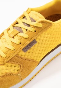 Gelbe Sneaker aus einer Mischung aus Netz- und Wildledermaterialien, braunen Akzenten, flachen gelben Schnürsenkeln und einer weißen Sohle mit gelben Details.
