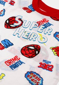 Biały materiał z czerwonym kołnierzem, ozdobiony czerwonymi maskami Spider-Mana, niebieskim i czerwonym tekstem o tematyce superbohaterów, błyskawicami oraz frazami takimi jak "SUPERBOHATER" i "WALCZY Z PRZESTĘPCZOŚCIĄ."