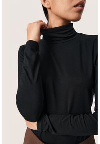 Mustmustööp, pikad varrukad, sile tekstuur, keha lähedane disain. Varrukad ulatuvad just randme kohale. Lihtne ja minimalistlik stiil.