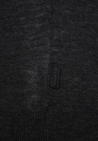 Dunkelgrauer Strickpulloverstoff mit glatter Textur. Ein kleines schwarzes Stoffetikett mit der Aufschrift "OLYMP" ist sichtbar.