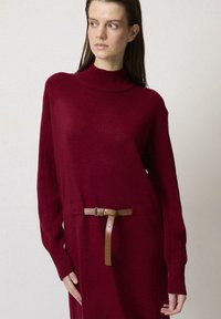 Rochie tricotată de culoare burgundă, cu guler înalt, mâneci ribbed și o curea din piele bej. Textură moale, croială lejeră și detalii pe laterale.