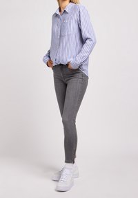 Camisa de botón a rayas azul y blanca, jeans ajustados grises con cremalleras en los tobillos, combinados con zapatillas blancas y calcetines blancos.