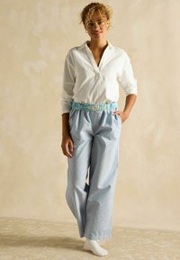 Biela košeľa s dlhým rukávom má golier; modro-bielo pruhované nohavice s širokými nohavicami, elastickým pásom a svetlomodrými akcentmi.