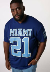 Blå trøje med "MIAMI" i fede lyseblå bogstaver og "21" på forsiden. Korte ærmer, v-hals design, glat stoftekstur.