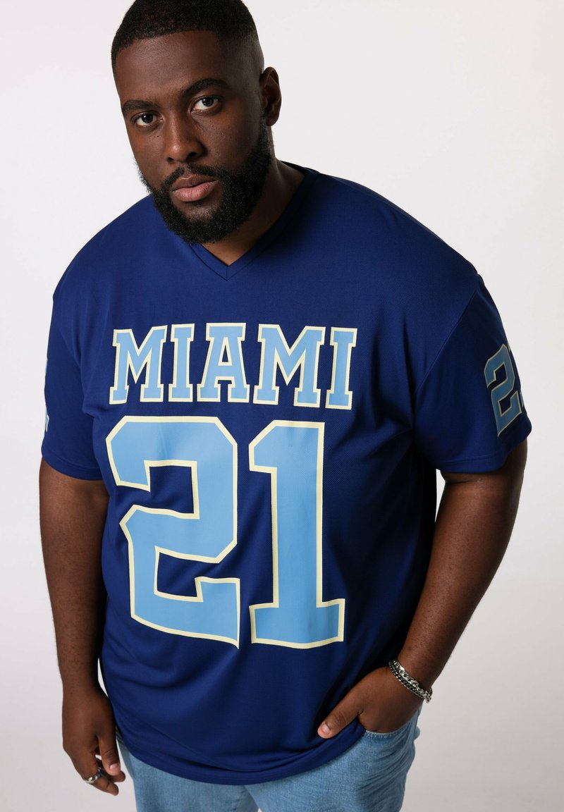 Blå trøje med "MIAMI" i fede lyseblå bogstaver og "21" på forsiden. Korte ærmer, v-hals design, glat stoftekstur.