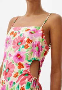 Vestido floral con escote cuadrado, con patrones en rosa, rojo y verde. Confeccionado en una tela ligera con cortes laterales y lazos ajustables.