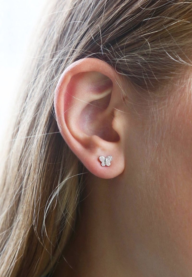 Zilveren vlinder studs met een textuur, versierd met kleine heldere rhinestones, gedragen op de oorlel.