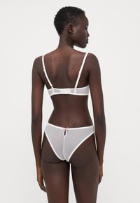Weiße Spitzen-Bralette und passende Tanga mit Tupfenmuster, weichem Material, verstellbaren Trägern und einem kleinen pinken Schleifenakzent.