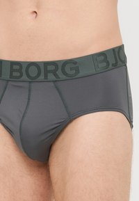 Pilkas trumpa stiliaus apatinis trikotažas, pagamintas iš lygaus audinio, su tamsiai žalia elastinga juosta, ant kurios yra "BORG" tekstas, ir prigludusia forma.